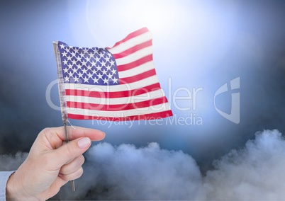 Composite image of hand holding little American flag against clouds