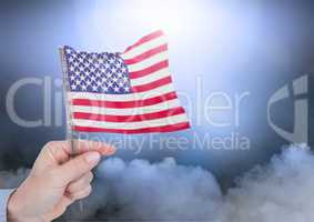 Composite image of hand holding little American flag against clouds