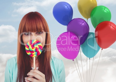 Composite image of red-headed woman with lollipop against colored balloons in sky