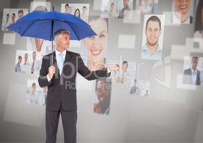 Businessman using an umbrella looking at photo wall against a grey background