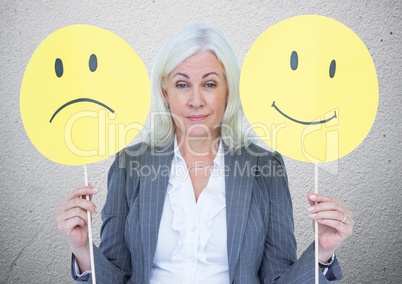 Senior businesswoman holding smileys against grey textured wall
