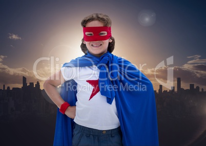 Boy in superhero costume standing with his hands on his hips against cityscape background