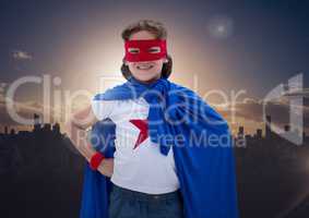 Boy in superhero costume standing with his hands on his hips against cityscape background