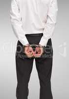 Rear view of corrupt businessman in handcuffs standing against white background