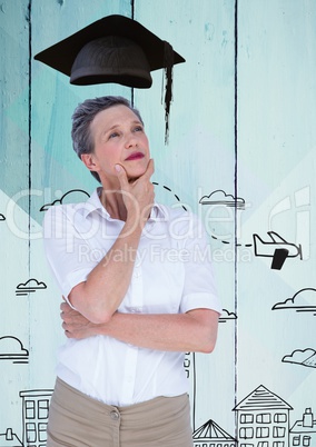 Thoughtful woman with graduation hat standing against hand drawn city on wooden background