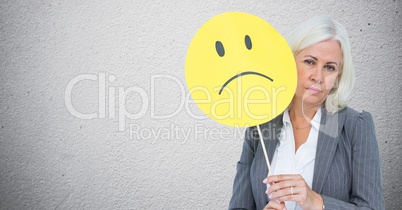 Senior businesswoman holding smiley face against grey background