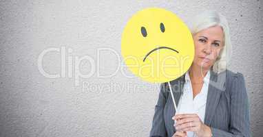Senior businesswoman holding smiley face against grey background