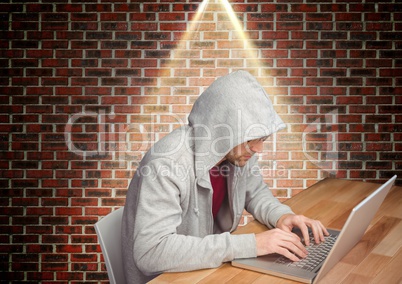 Man in hooded top sitting against brick wall and using laptop