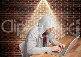 Man in hooded top sitting against brick wall and using laptop