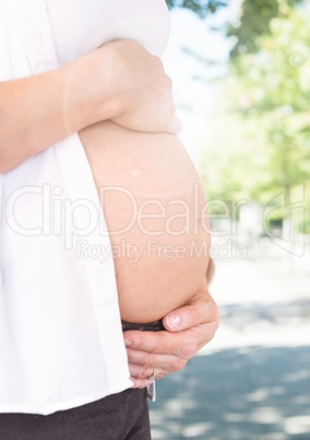 Mid section of pregnant woman holding her belly against greenery