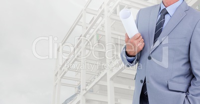 Businessman holding blueprints against construction site in background
