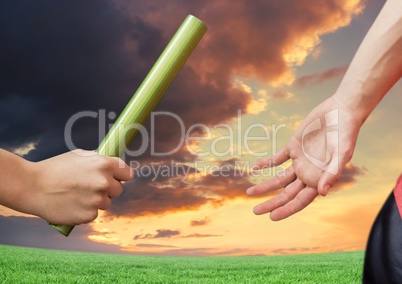 Athlete passing the baton to teammate against dramatic sunset background