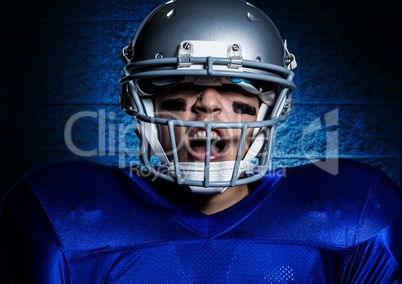 Aggressive american football player in helmet screaming against blue wall background