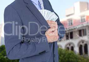 Mid section of businessman hiding money in blazer against house