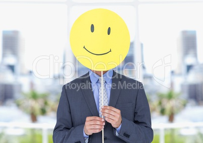 Businessman holding happy smiley face in front of her face against office in background