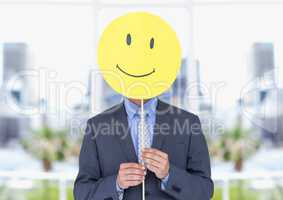 Businessman holding happy smiley face in front of her face against office in background