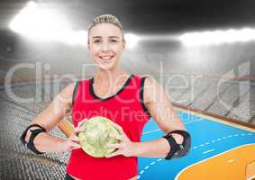 Portrait of happy female handball player holding ball with stadium in background