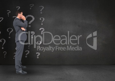 Thoughtful businessman standing with question marks in background