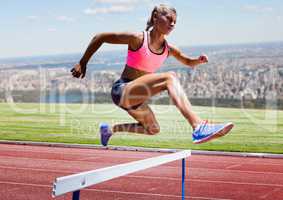 Athlete running over hurdle in stadium