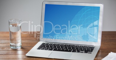 Laptop and glass of water on wooden table in office