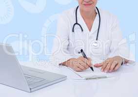 Female doctor sitting at desk with laptop and writing on clipboard