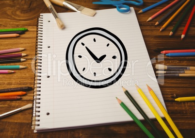 Hand drawn alarm clock on spiral note book and multi colored crayon wooden table
