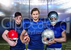 American football players holding helmets and ball against stadium in background