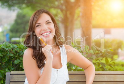 Young Adult Female Student with Pencil on Bench Outdoors
