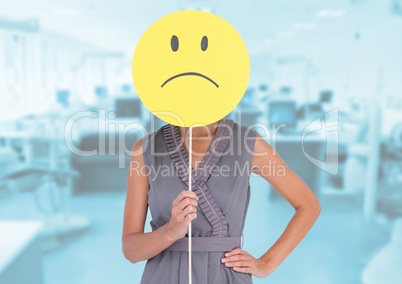 Businesswoman holding sad smiley face in front of her face against office in background