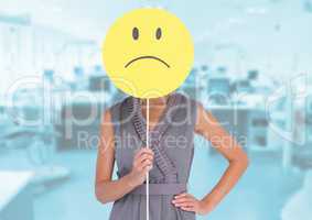 Businesswoman holding sad smiley face in front of her face against office in background