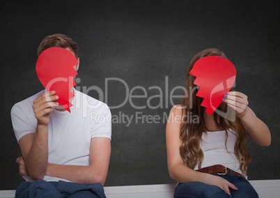 Depressed couple holding broken heart against grey background