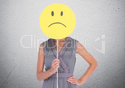 Woman covering her face with sad smiley against concrete background