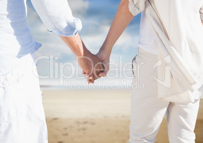Mid section of couple holding hands and walking on beach