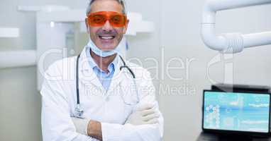 Portrait of smiling doctor in protective eyewear standing with arms crossed