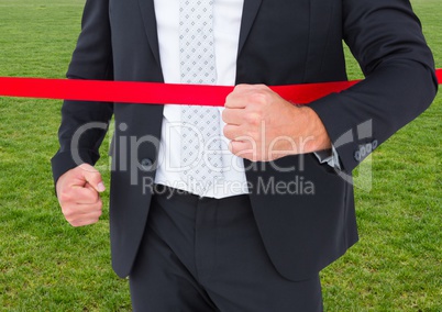 Businessman crossing finish line against green grass