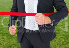 Businessman crossing finish line against green grass