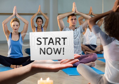 Hand holding placard that reads start now against people doing meditation