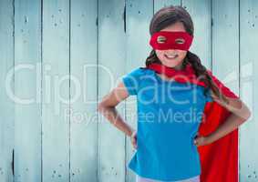 Girl in superhero costume with hands on her hip standing against against wooden background