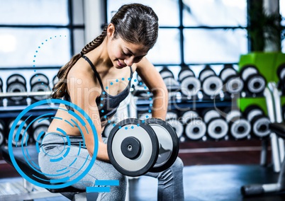 Fit woman performing bicep curl exercise in gym against digital fitness interface