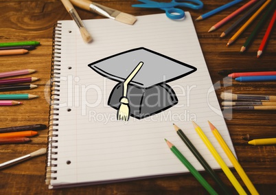 Drawn mortar board on notebook with color pencils on wooden table