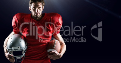 American football player holding helmet and ball against black background