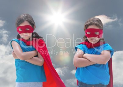 Kids in superhero costumes standing with arms crossed against sky in background
