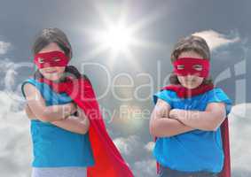 Kids in superhero costumes standing with arms crossed against sky in background