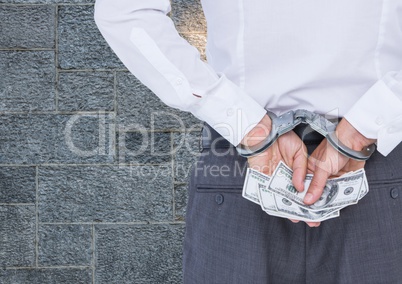 Corrupt businessman in handcuffs holding money against wall
