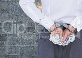 Corrupt businessman in handcuffs holding money against wall