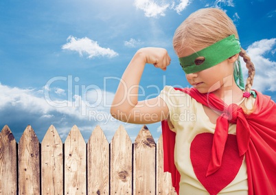 Girl in in superhero costume flexing her arms against sky in background