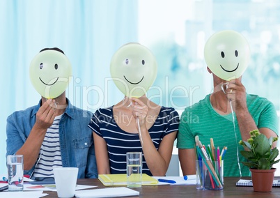 Colleagues holding smiley while sitting on desk