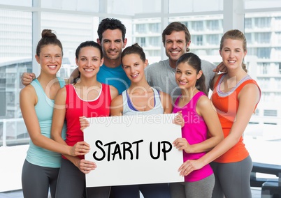 Fit men and women holding placard with start up text in fitness studio