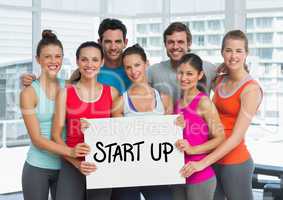Fit men and women holding placard with start up text in fitness studio