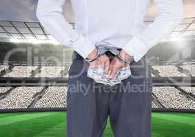 Corrupt businessman in handcuffs holding money at stadium